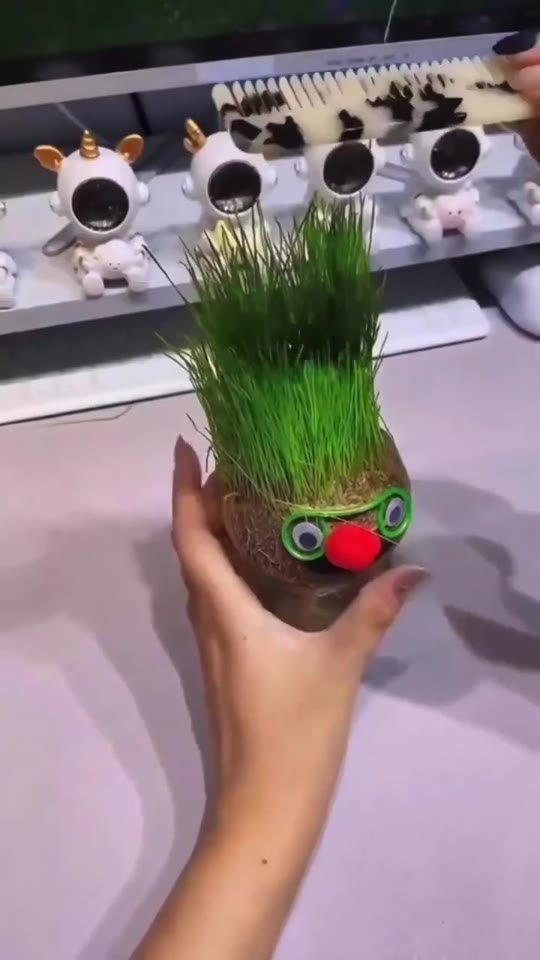 Boneco ecológico real com cabelo de grama, óculos verdes e nariz vermelho, segurado por uma mão
